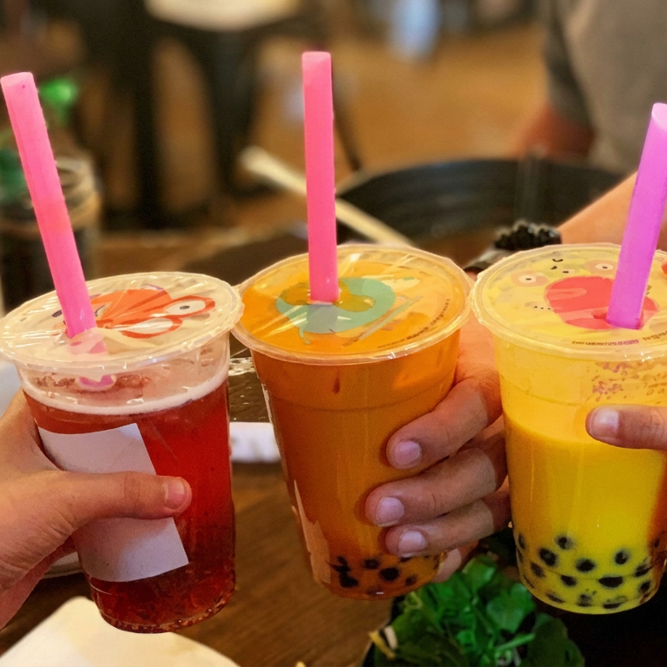 Three colorful bubble tea drinks with pink straws held together over a restaurant table.
