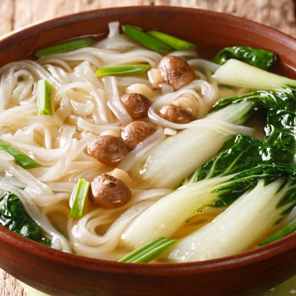 Bowl of translucent noodles in broth with bok choy, mushrooms, cabbage, and green onions on a rustic wooden table.