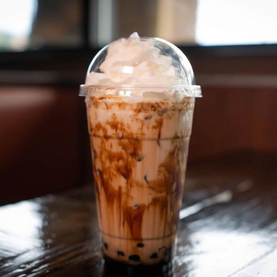 Caramel-drizzled iced milk tea with tapioca pearls and whipped topping in a clear cup on a restaurant table.